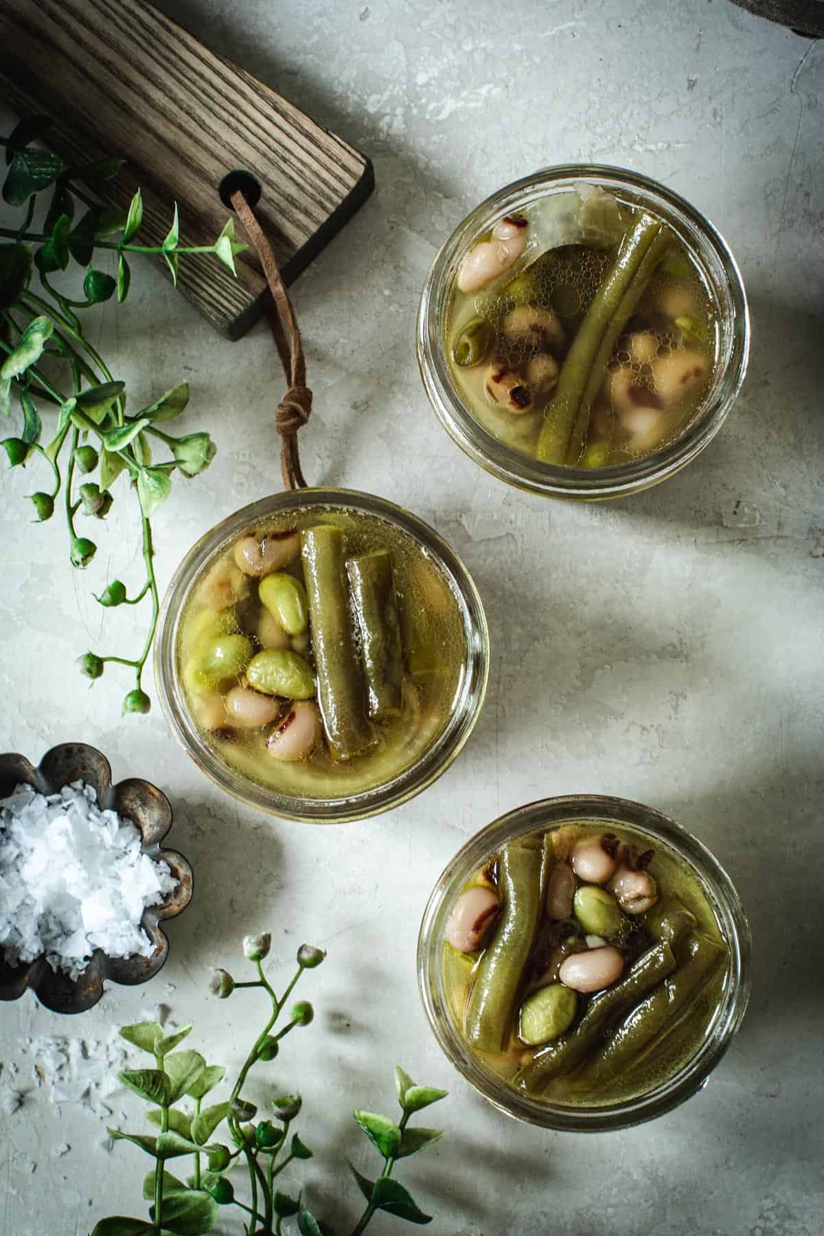 Pickled three bean salad in three small jars with salt in a tin sitting next to it.