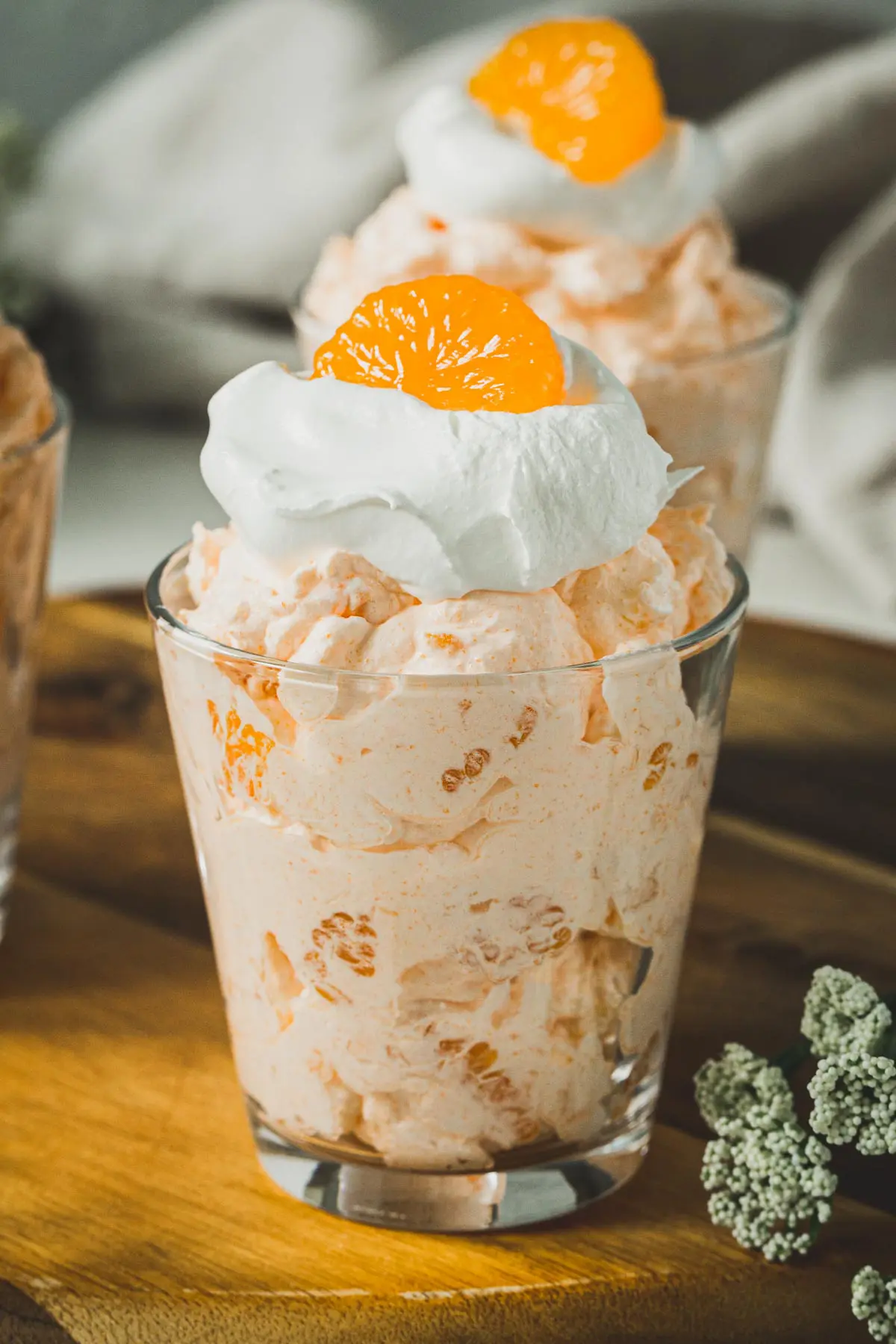 Orange jello salad in a glass jar topped with whipped cream and an orange wedge.