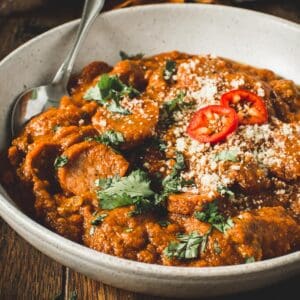 Sausage pumpkin chili in a white bowl with a silver spoon.