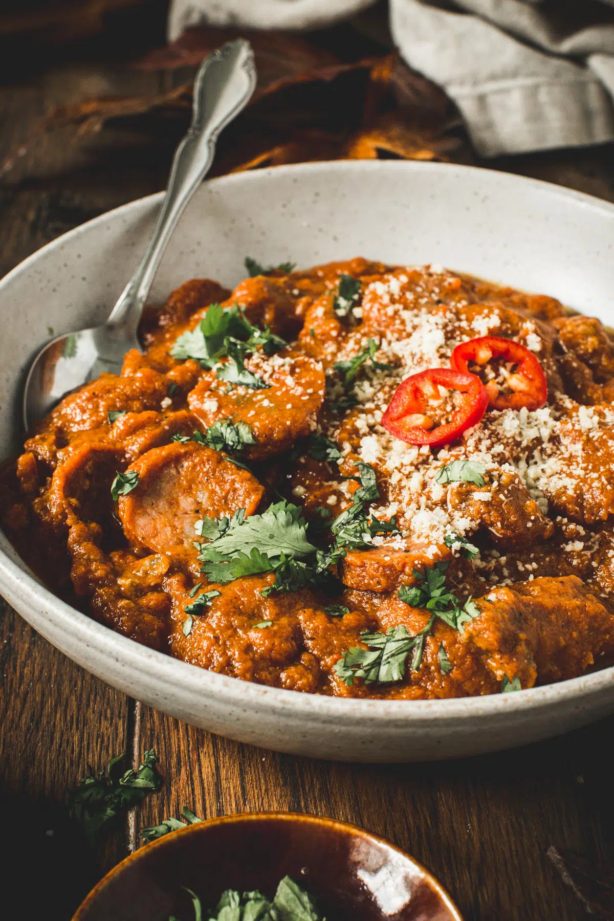 Sausage pumpkin chili in a white bowl with a silver spoon.