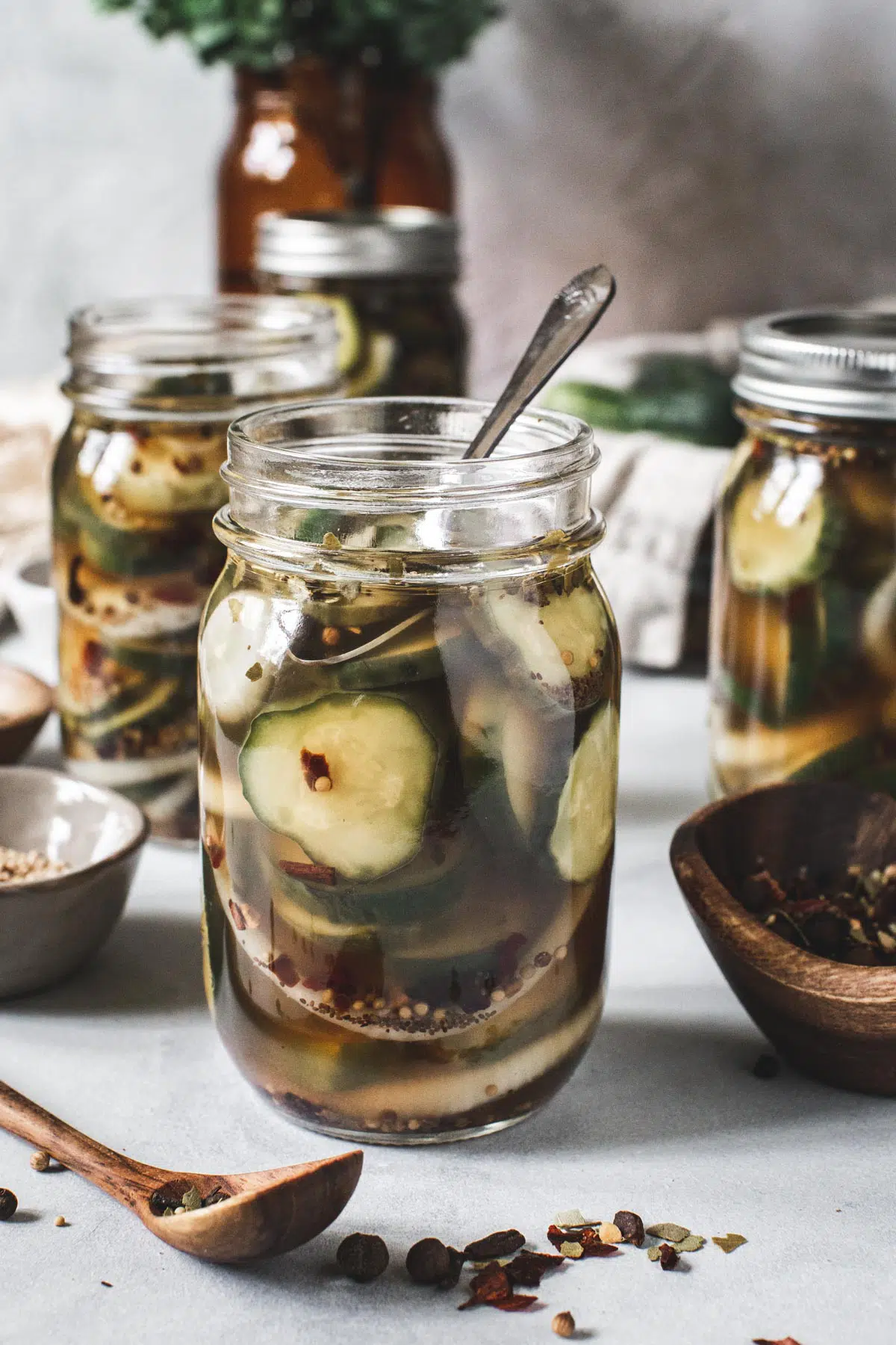 Refrigerator bread and butter pickles in mason jars with spices surrounding them.