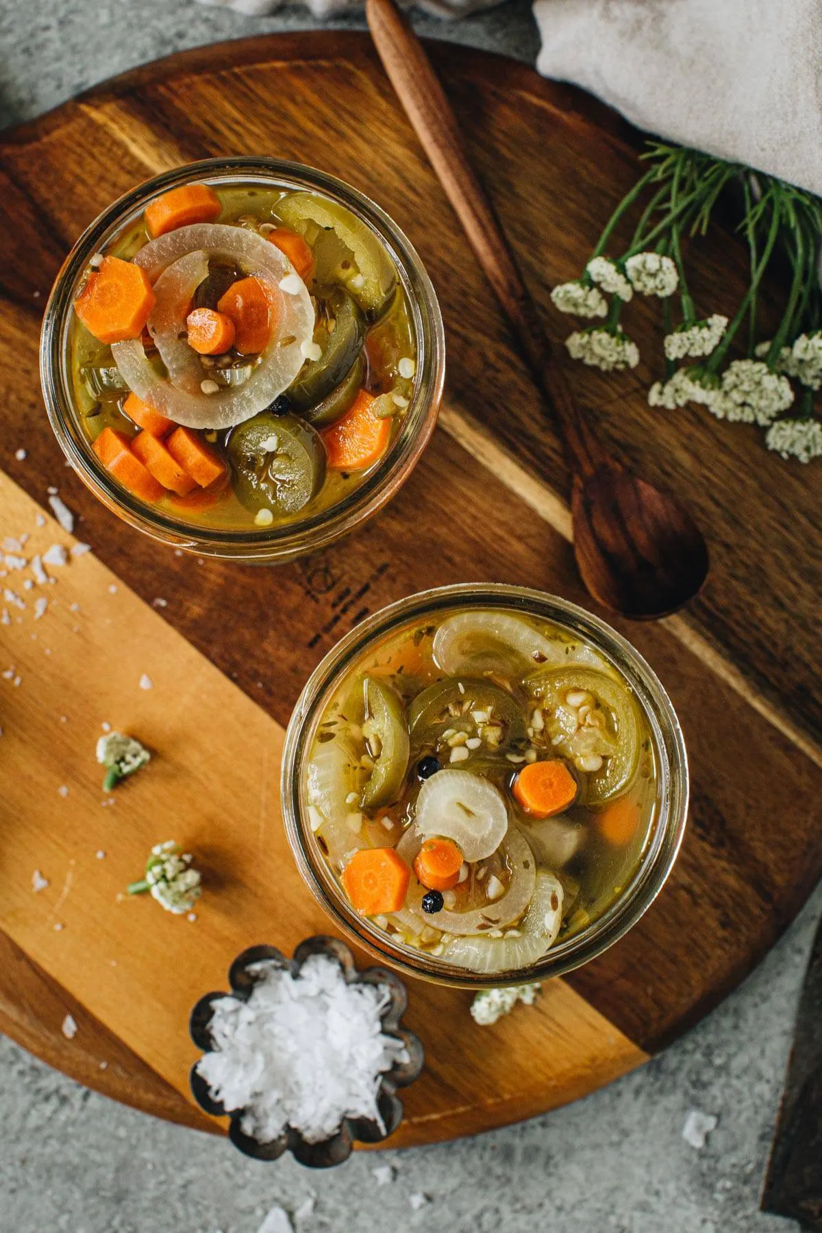 Escabeche in wide mouth pine jars sitting on a wooden cutting board.