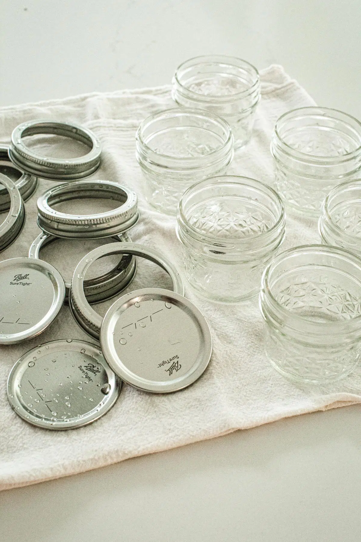 Canning jars, lids, and rings drying on a white towel.