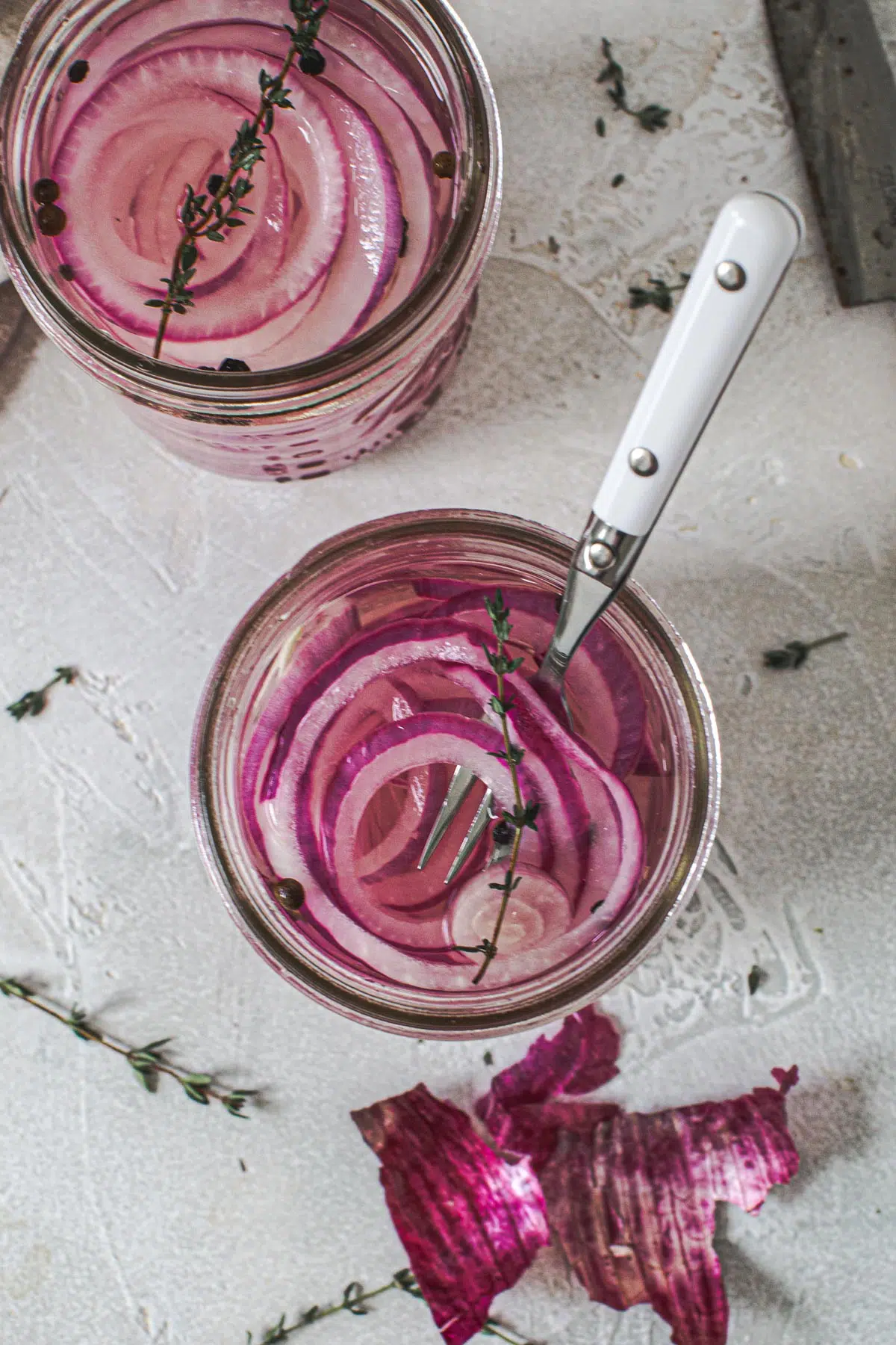 Quick pickled red onions in a jar with fresh thyme on top and a white serving fork.
