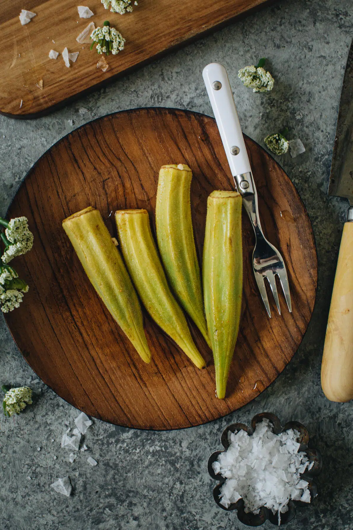 Pickled okra on a wooden plate with a white serving fork.