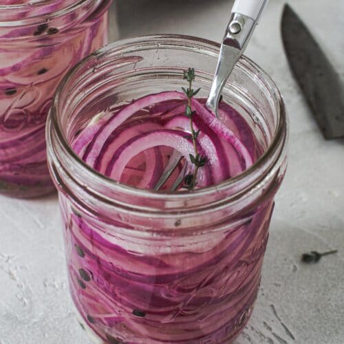 Quick pickled red onions in a pint jar with a white serving fork.