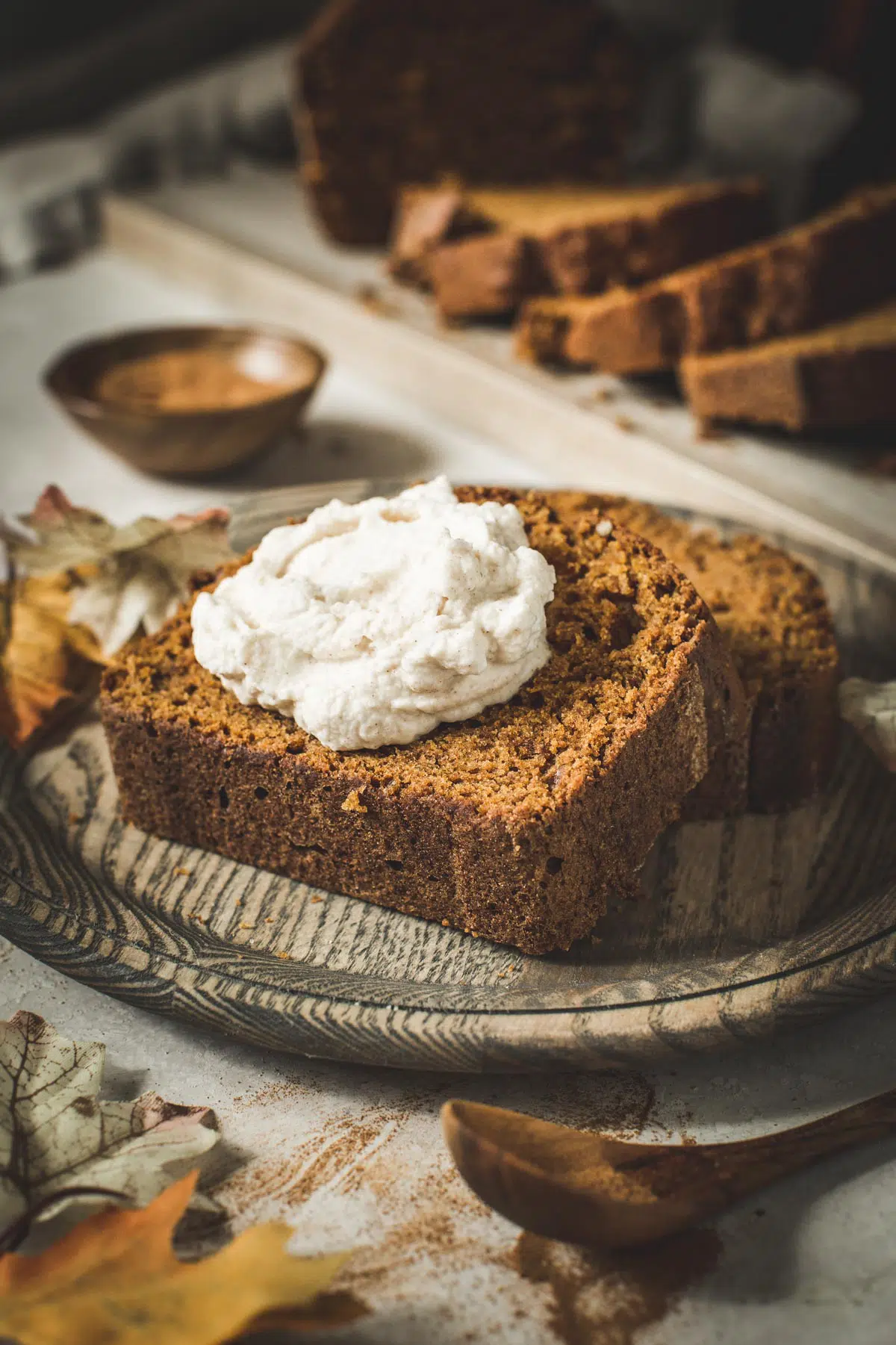 Moist pumpkin bread slice topped with whipped cream on a wooden plate.