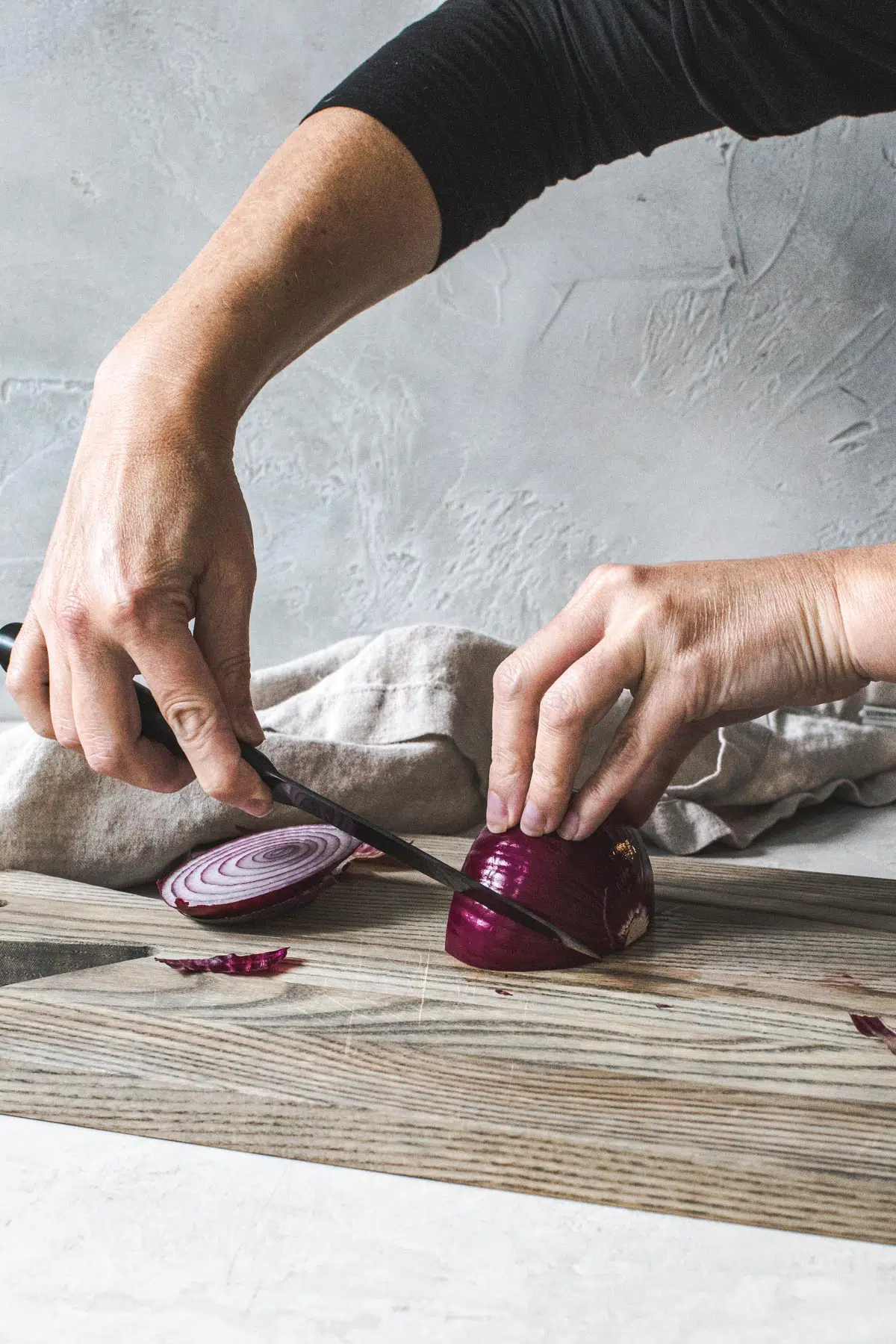 Hands holding and slicing an onion on a cutting board.