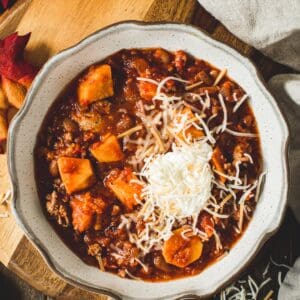 Sweet potato turkey chili with shredded cheese and sour cream on top in a bowl.