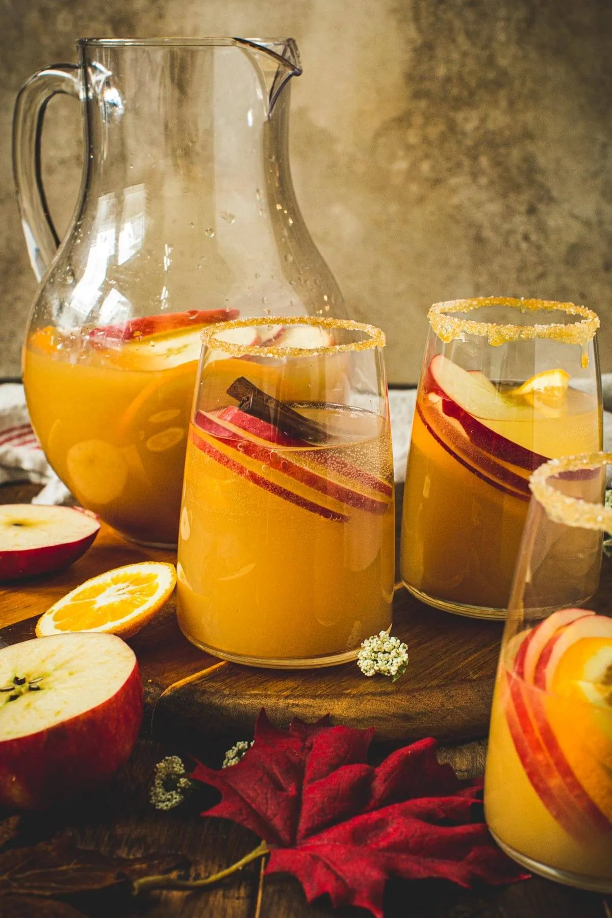 Three glasses filled with caramel apple sangria with a pitcher sitting behind.