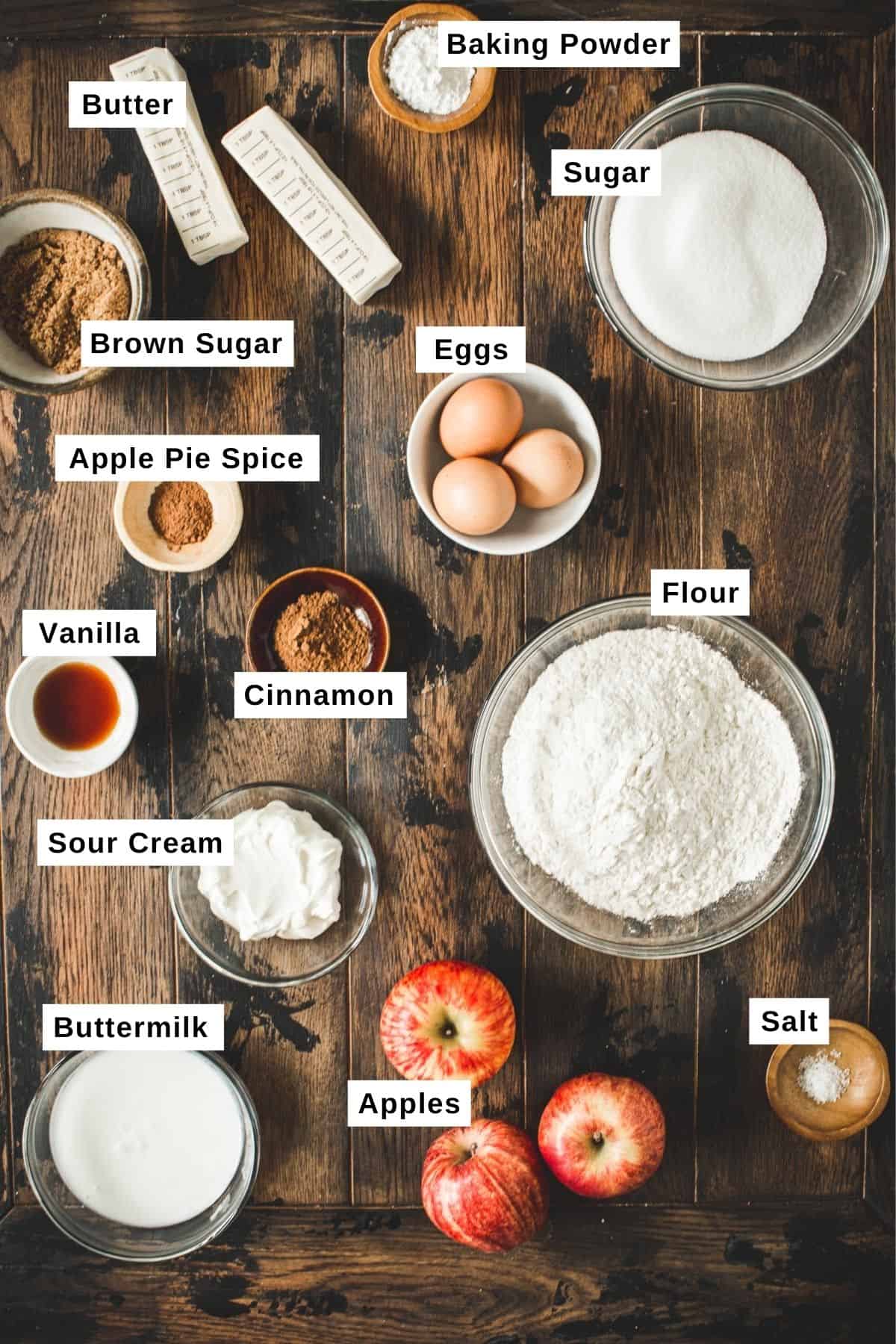 Apple crumble muffins ingredients in different bowls on a wooden table.