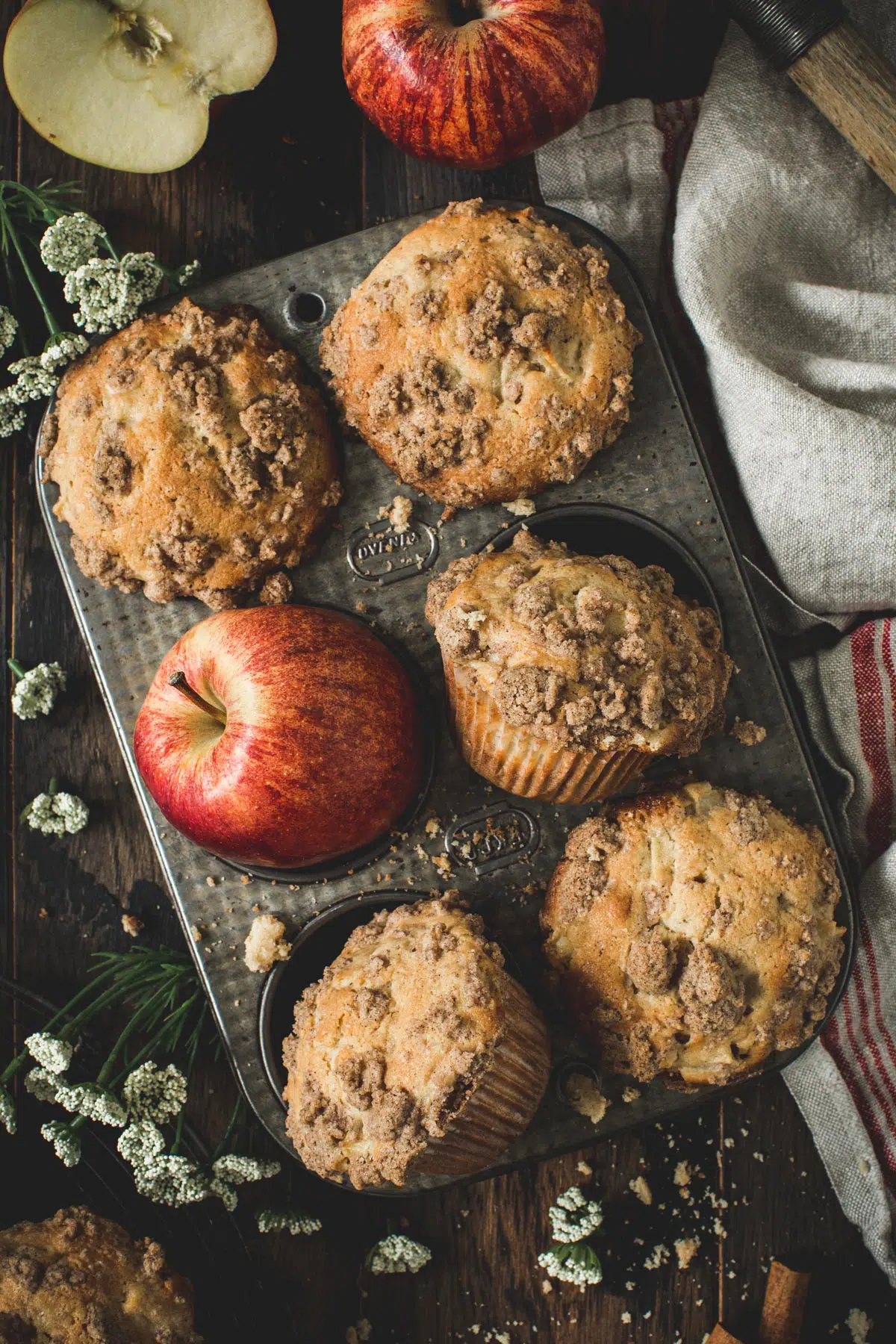 Apple crumble muffins in a muffin tin surrounded by crumbs.