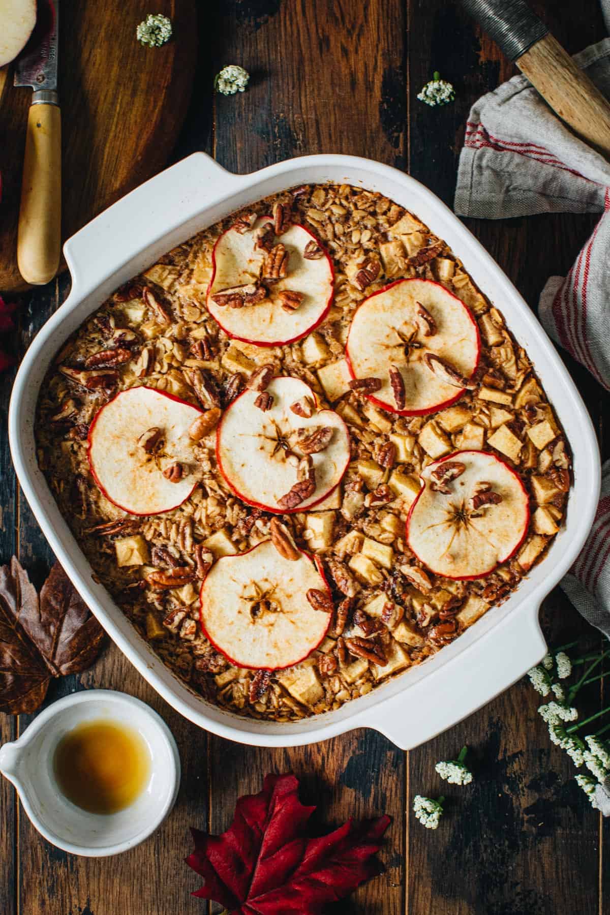 Baked apple oatmeal topped with pecans in a square baking dish.