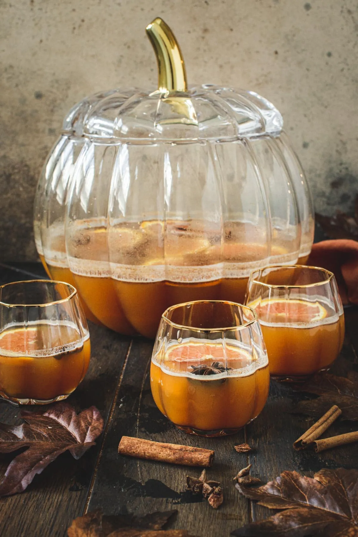 Halloween pumpkin punch cocktails in pumpkin-shaped glasses with orange slices and star anise on top.