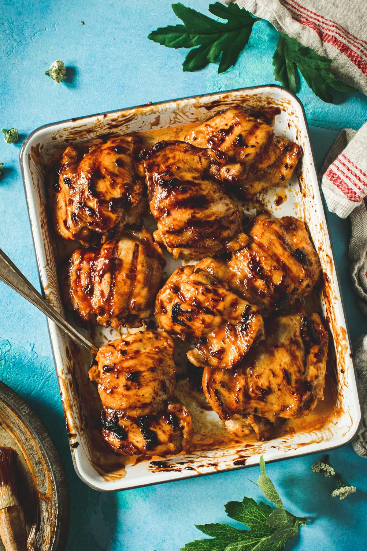 Huli huli chicken on a rimmed baking sheet with serving fork.