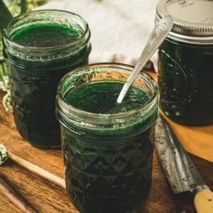 Jalapeno pepper jelly in a glass jar with a silver serving spoon.