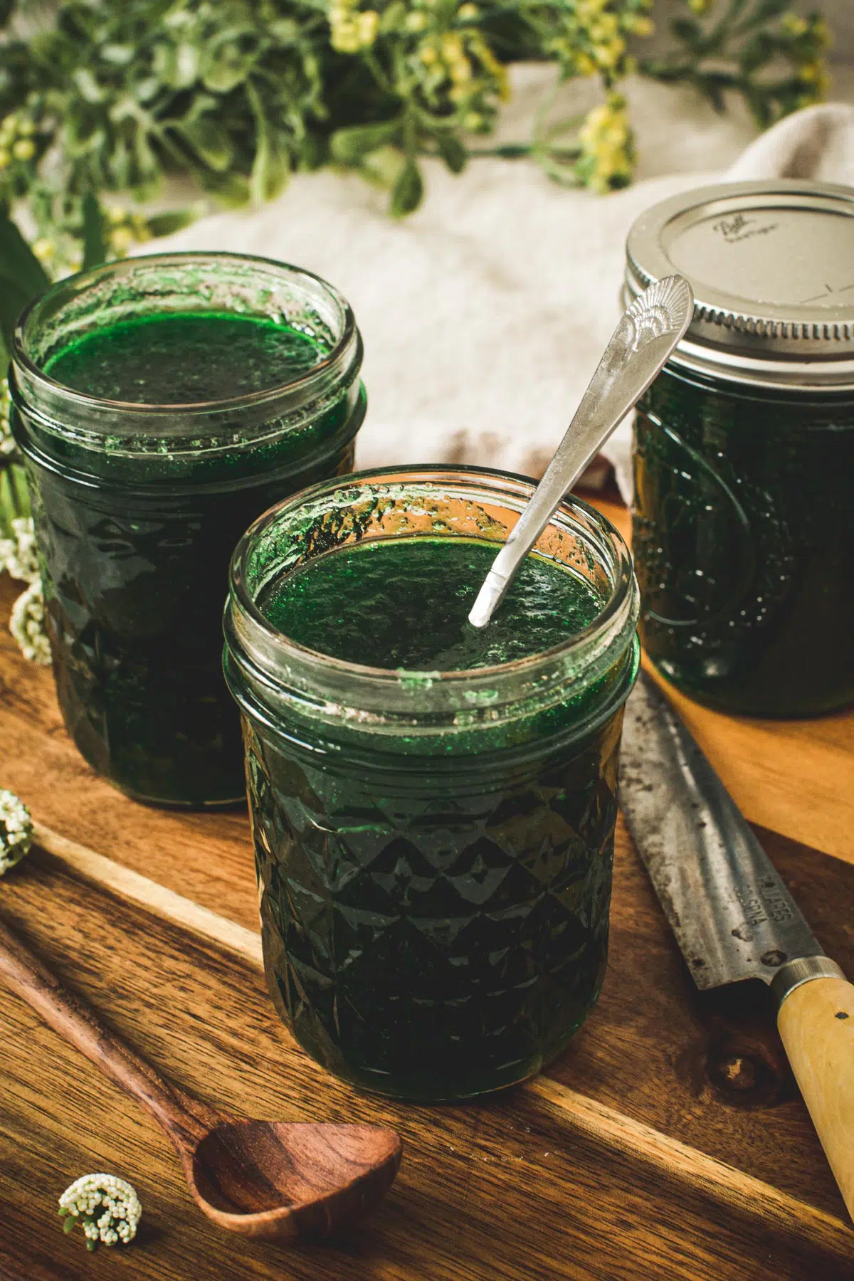 Jalapeno pepper jelly in a glass jar with a silver serving spoon inside.