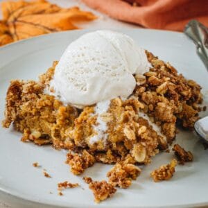 Pumpkin crisp topped with vanilla ice cream on a white plate.