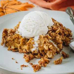Pumpkin crisp topped with vanilla ice cream on a white plate.