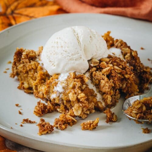 Pumpkin crisp topped with vanilla ice cream on a white plate.