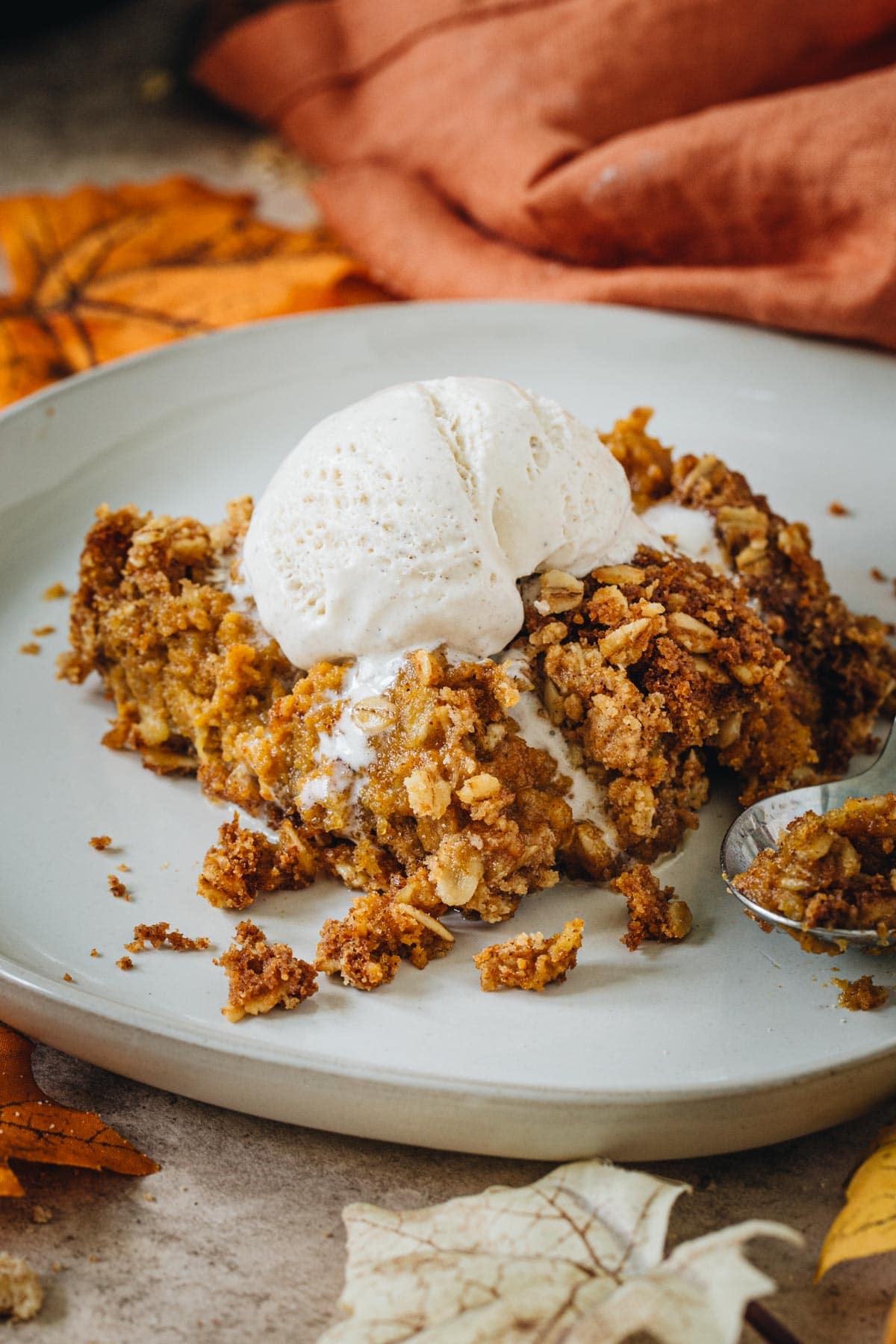 Pumpkin crisp topped with melting vanilla ice cream on a white plate.