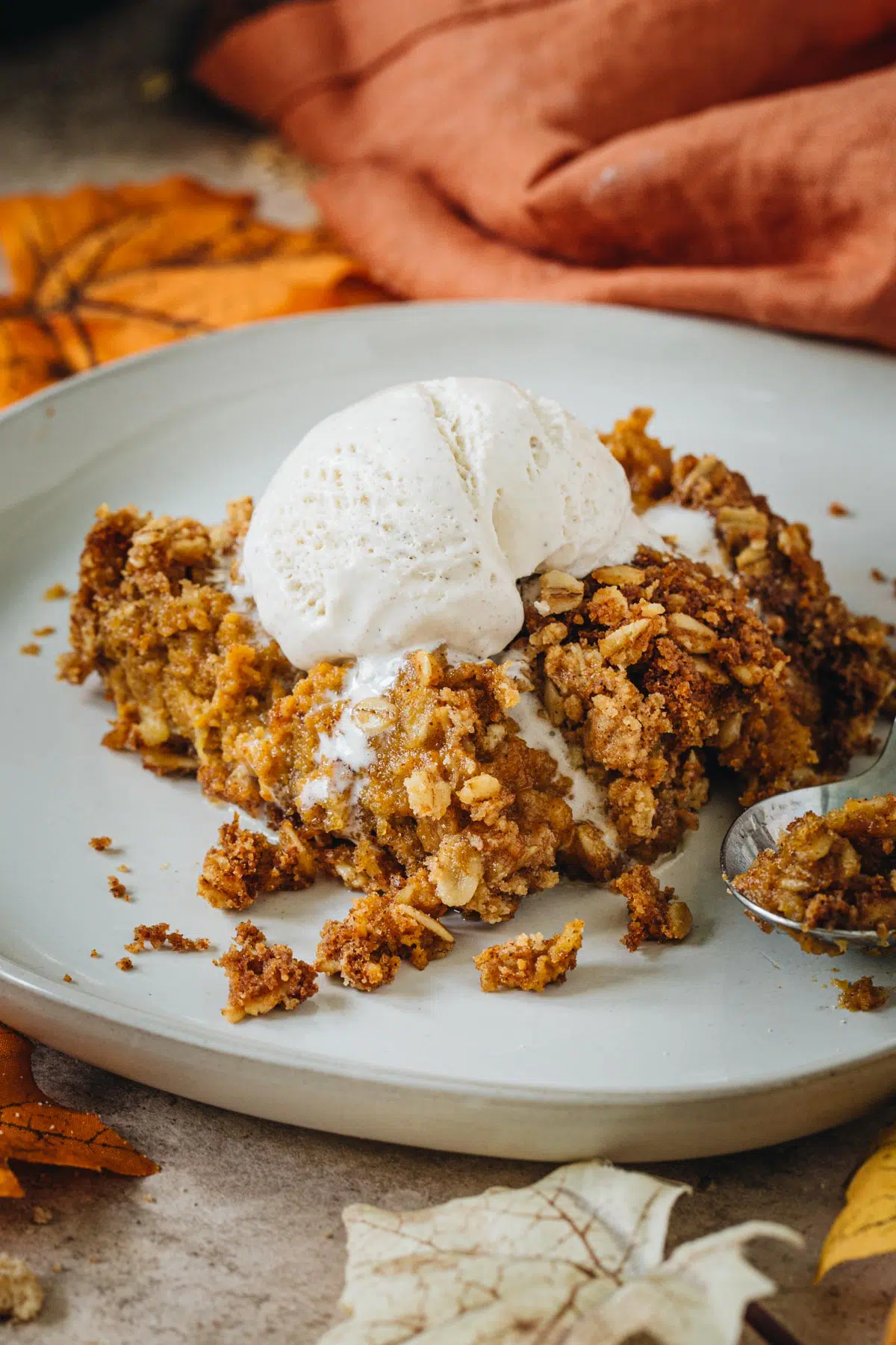 Pumpkin crisp topped with vanilla ice cream on a white plate.
