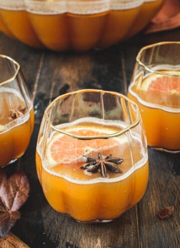 Pumpkin cocktail in a pumpkin-shaped glass topped with star anise and orange slices.