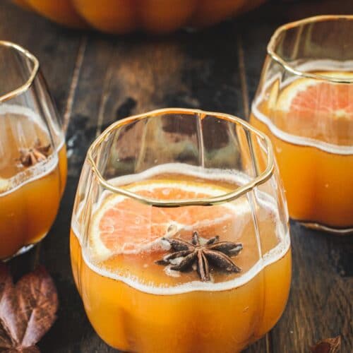 Pumpkin cocktail in a pumpkin-shaped glass topped with star anise and orange slices.