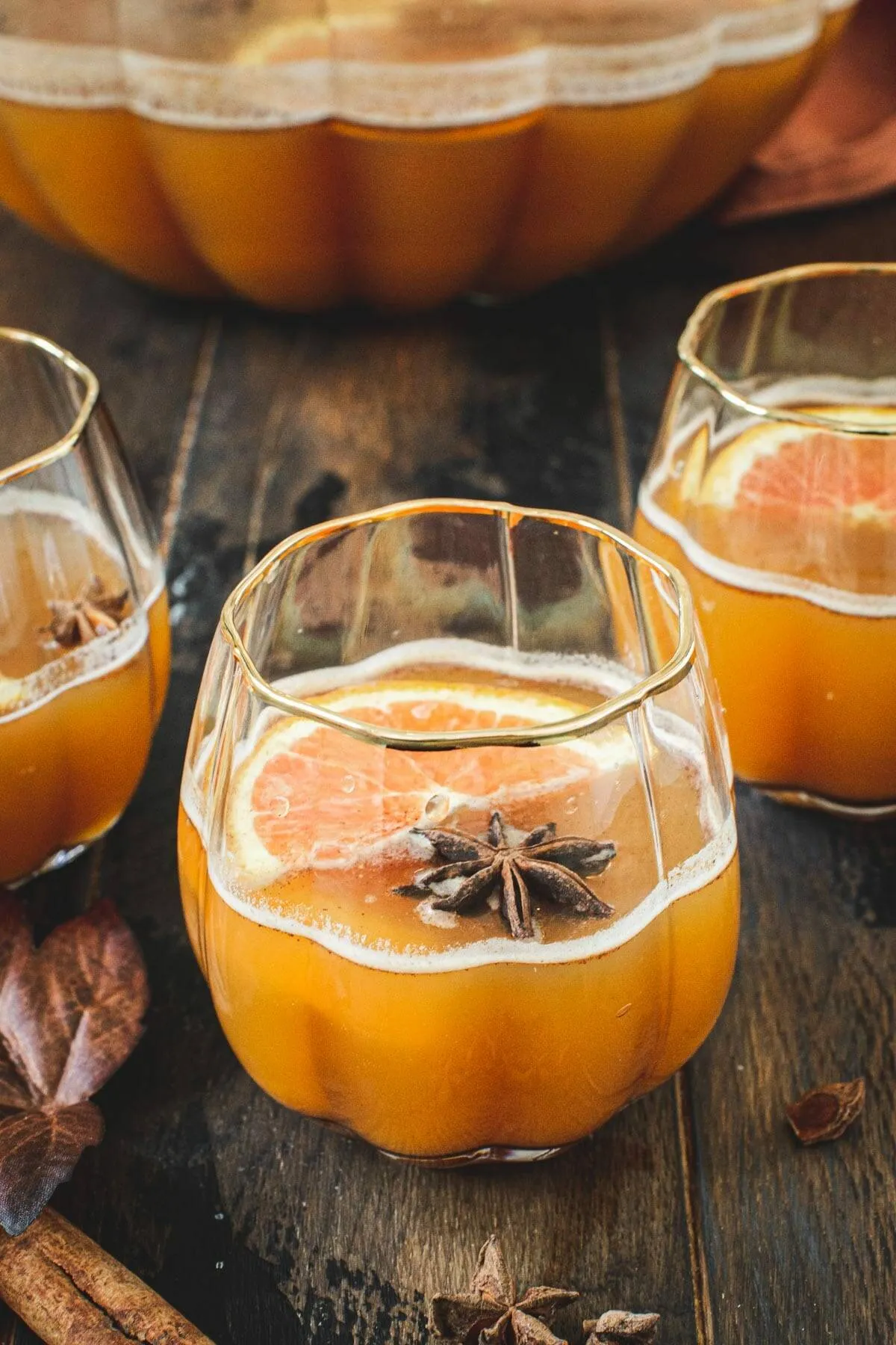 Pumpkin cocktail in a pumpkin-shaped glass topped with star anise and orange slices.