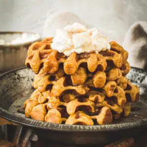 Stack of pumpkin spice waffles with whipped cream on top.