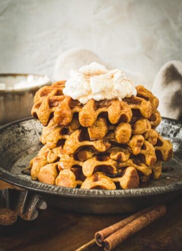 Stack of pumpkin spice waffles with whipped cream on top.