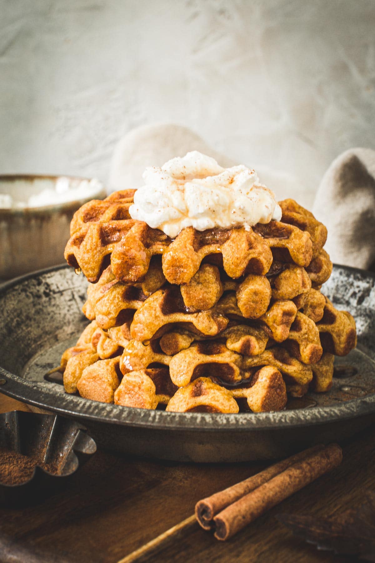 Stack of pumpkin spice waffles topped with whipped cream and syrup.