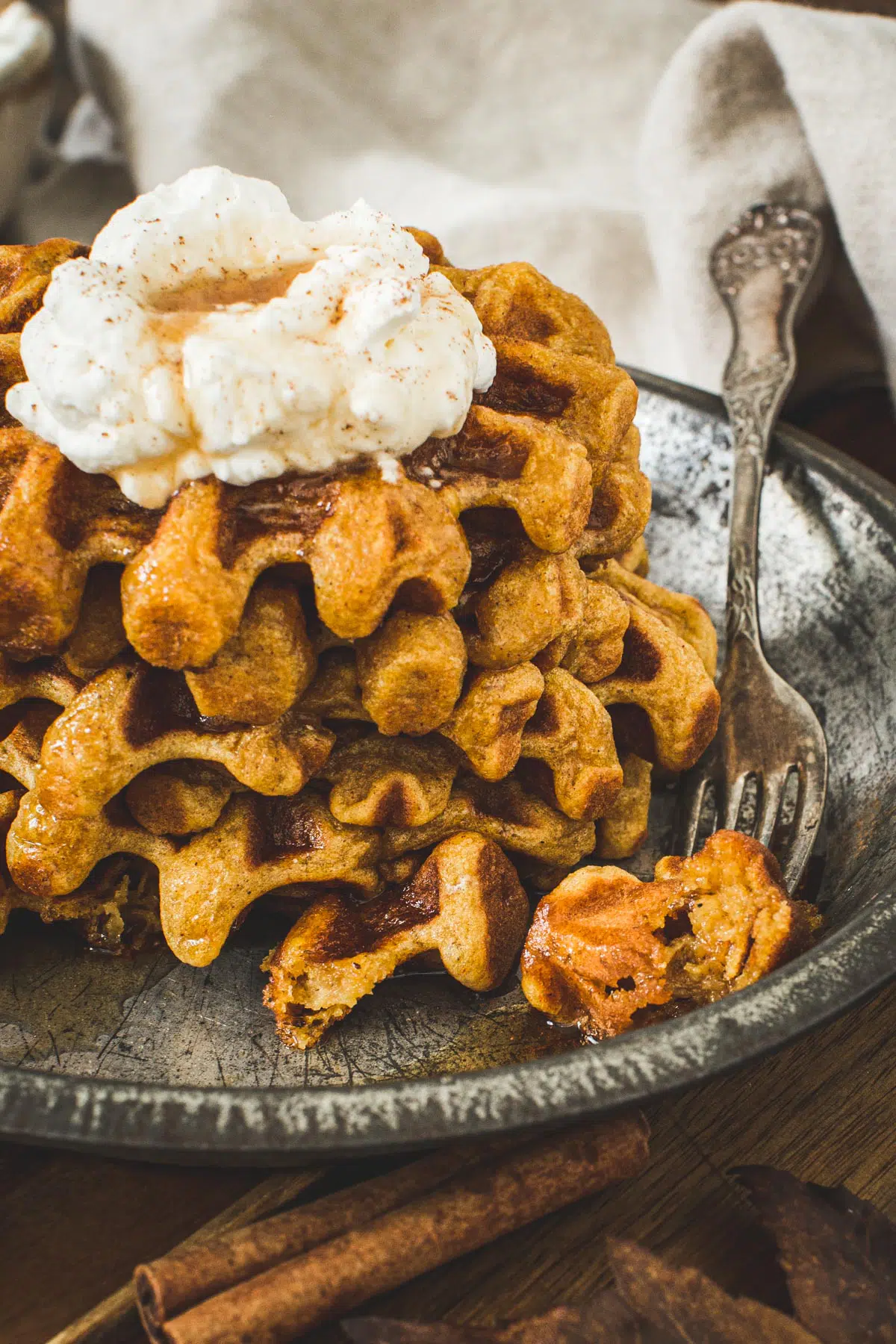 Fork with a piece of waffle sitting next to a stack of waffles.