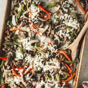 Homemade cheesesteak fajitas on a sheet pan with a wooden spoon.