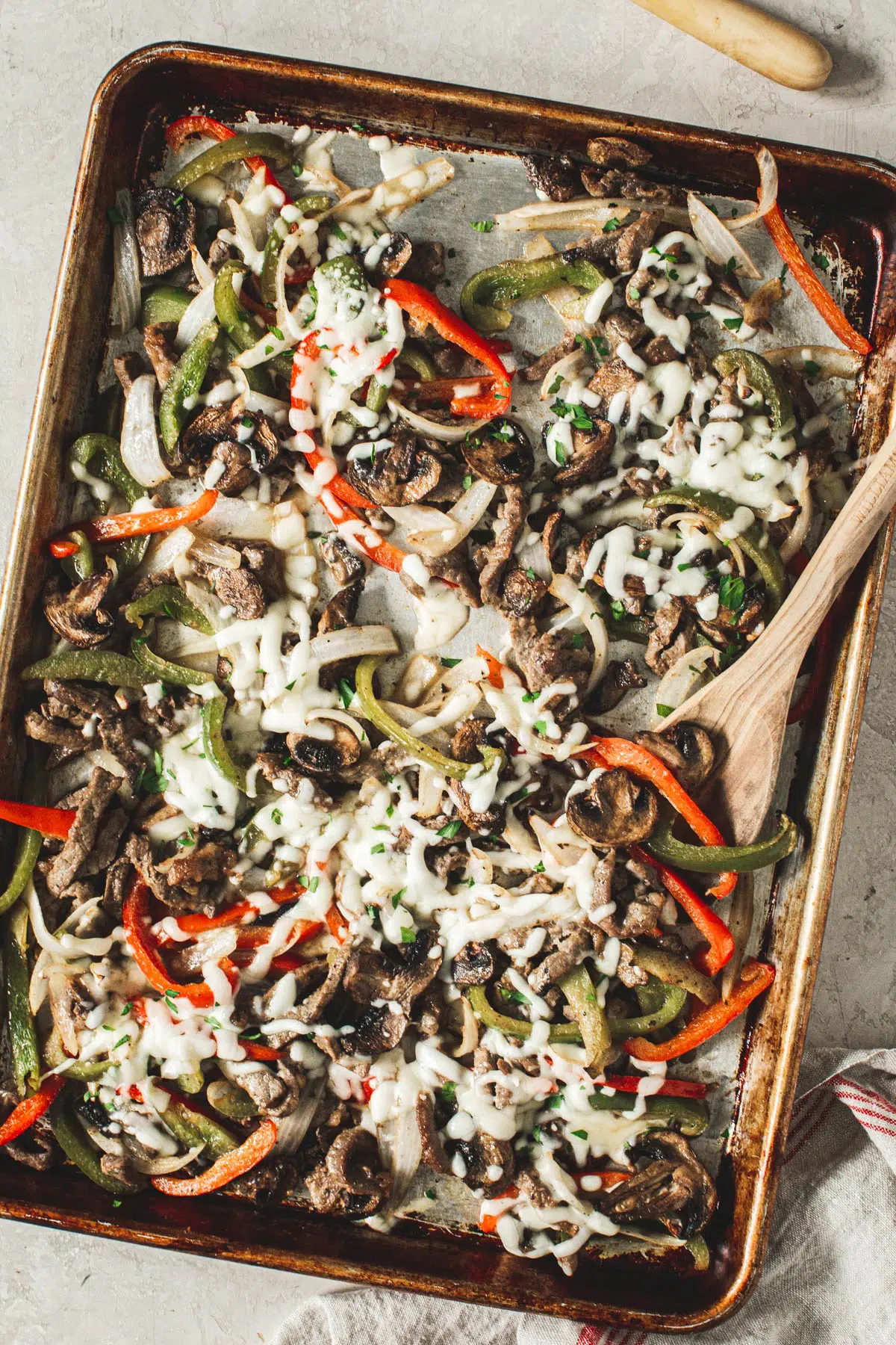 Homemade cheesesteak fajitas on a sheet pan with a wooden spoon.