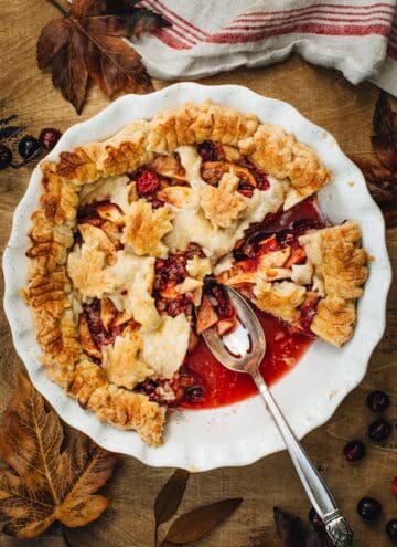 Apple cranberry pie with a slice removed in a white pie dish.