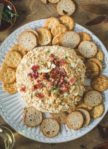 Bacon ranch cheese ball on a white plate with crackers surrounding it.