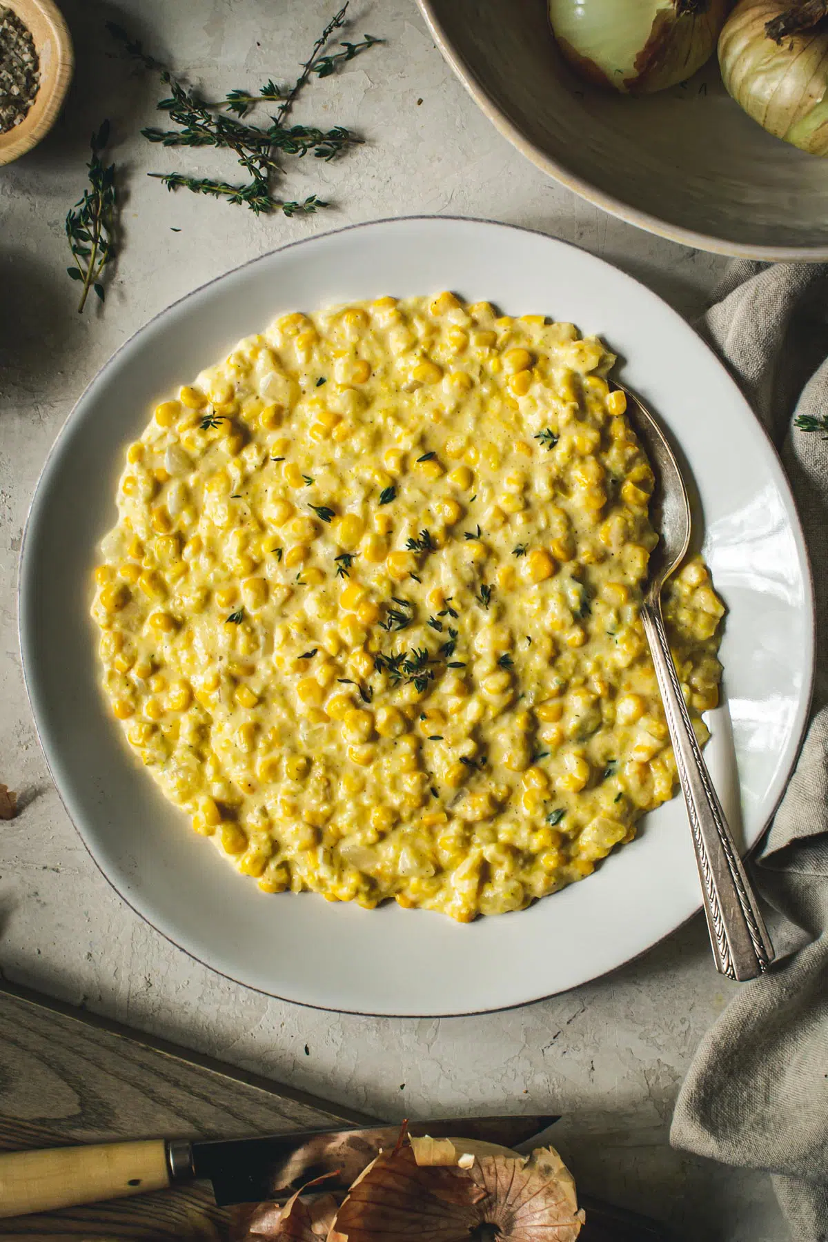 Creamed corn in a white bowl with fresh thyme on top.