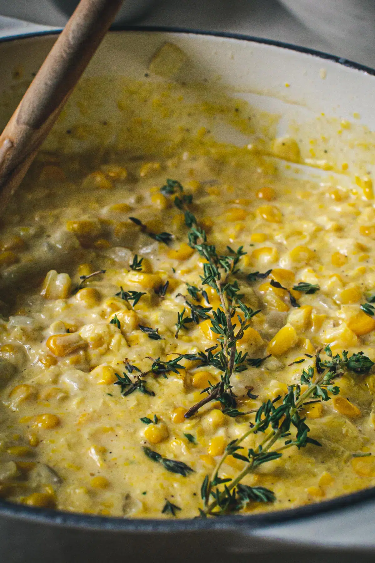 Creamed corn topped with fresh thyme in a white Dutch oven.