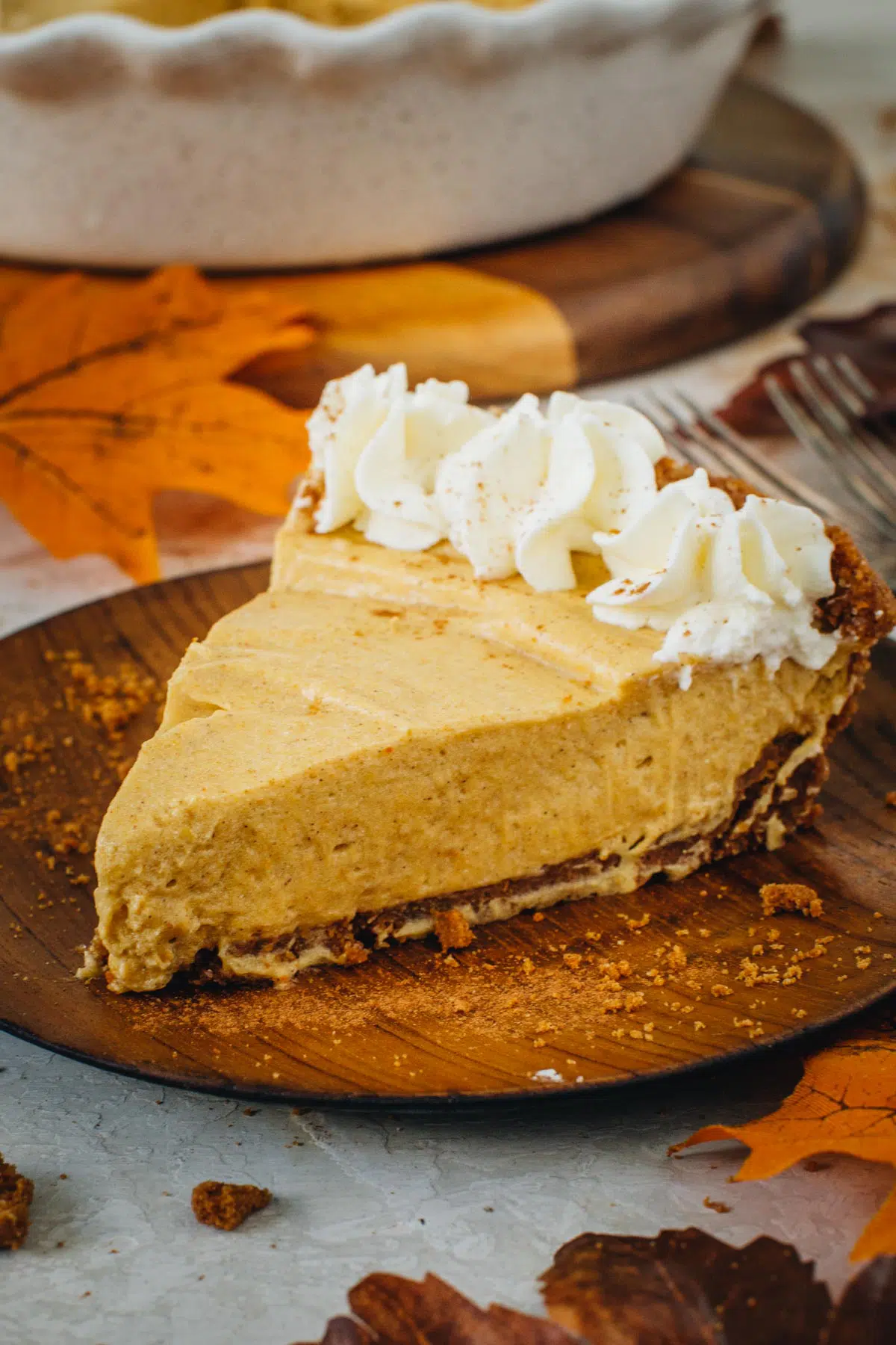 No-bake pumpkin pie slice with whipped cream on a wooden plate.