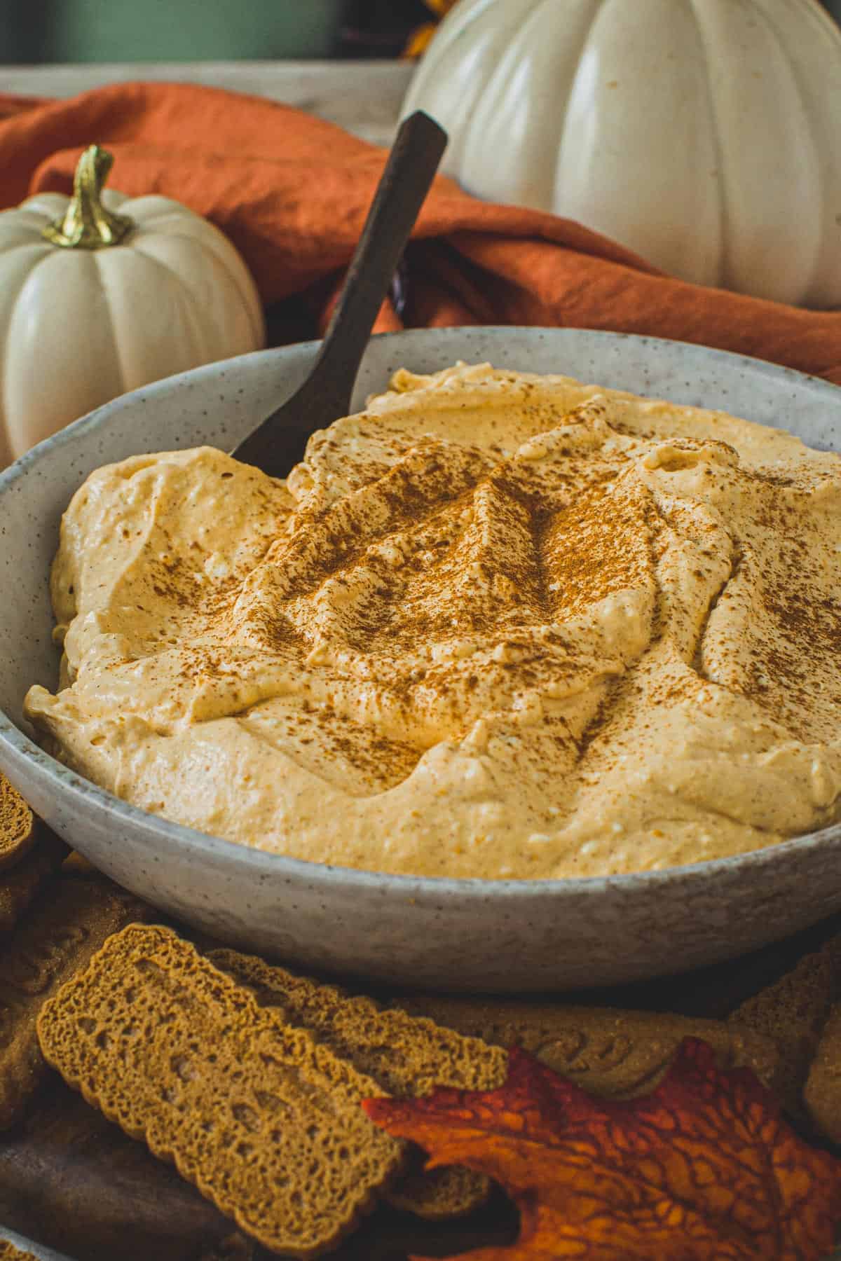 Pumpkin pie cheesecake dip topped with cinnamon in a bowl with a wooden spoon.