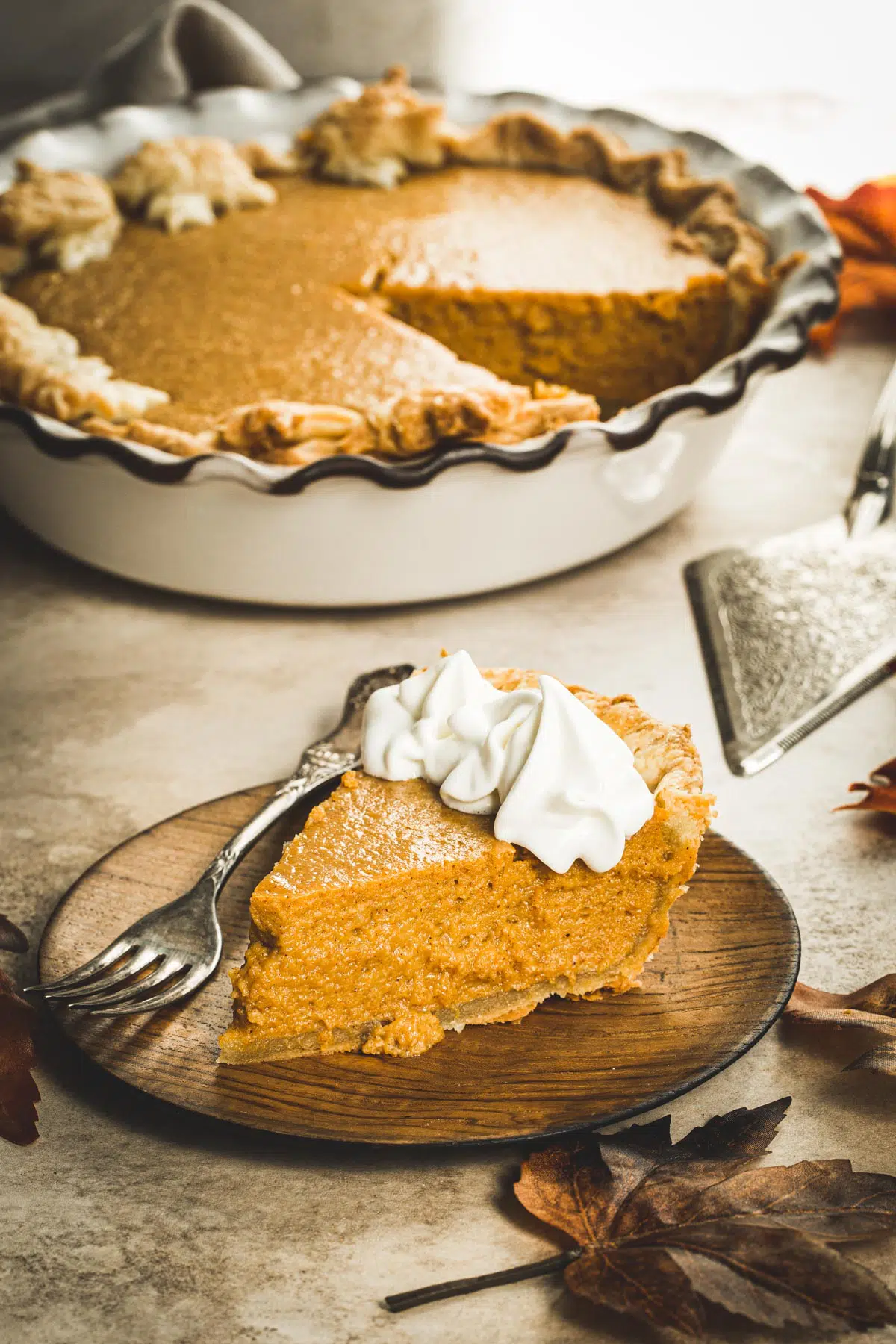 Slice of maple pumpkin pie with whipped cream on the edges.