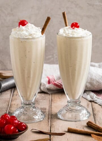 Eggnog milkshakes in glasses topped with whipped cream and cherries.