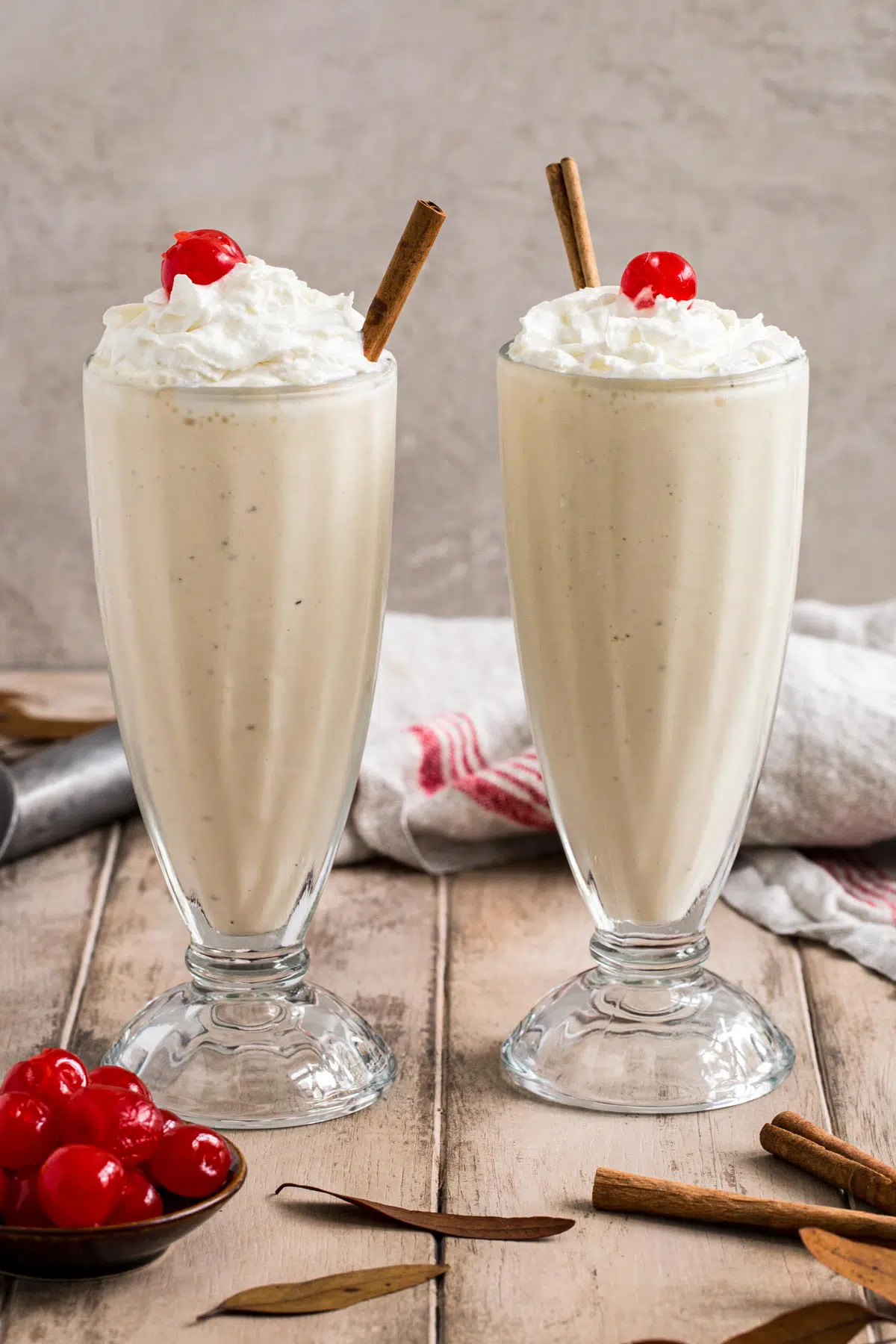 Two eggnog milkshakes in glasses topped with whipped cream and cherries.