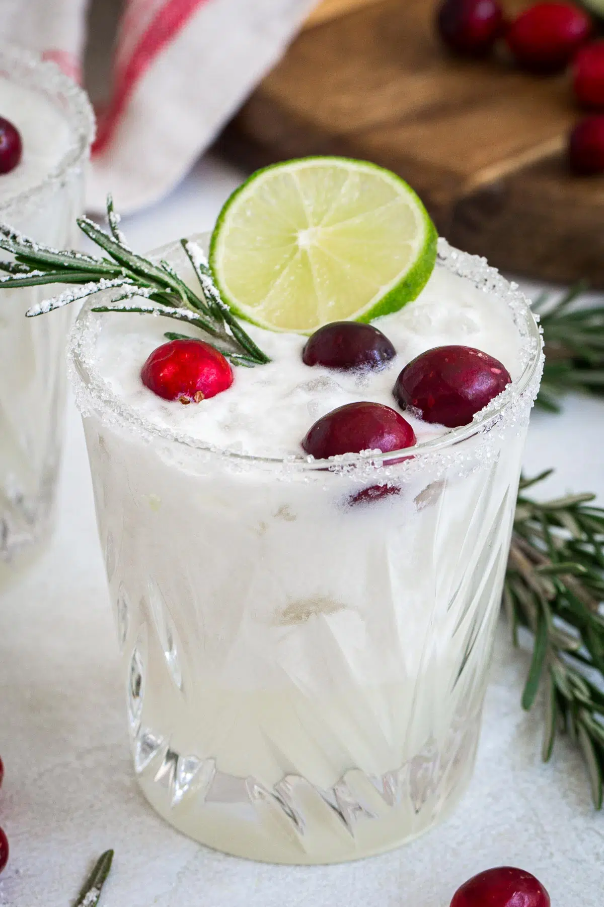 White Christmas margarita topped with fresh cranberries, sugared rosemary, and with a sugared rim.