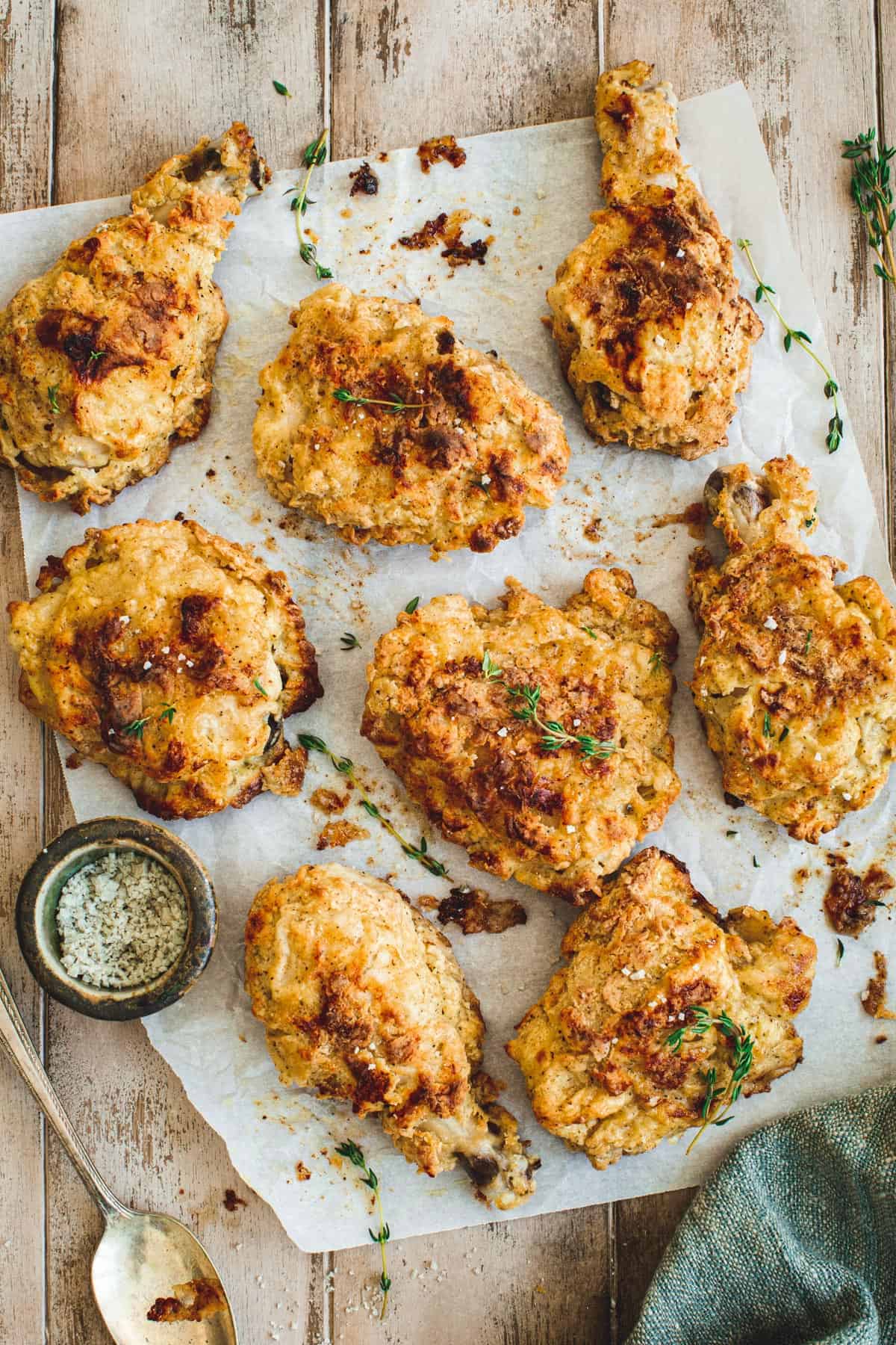 Southern oven-fried chicken on parchment paper with fresh thyme and coarse salt sprinkled on top.