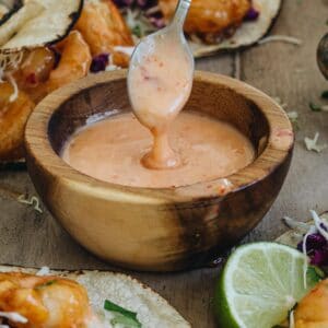 Bang bang sauce dripping off a spoon into a bowl of sauce.