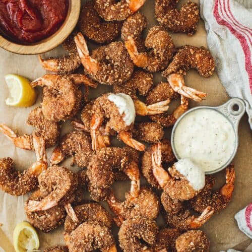 Crispy breaded shrimp piled on parchment with cocktail sauce and tartar sauce.