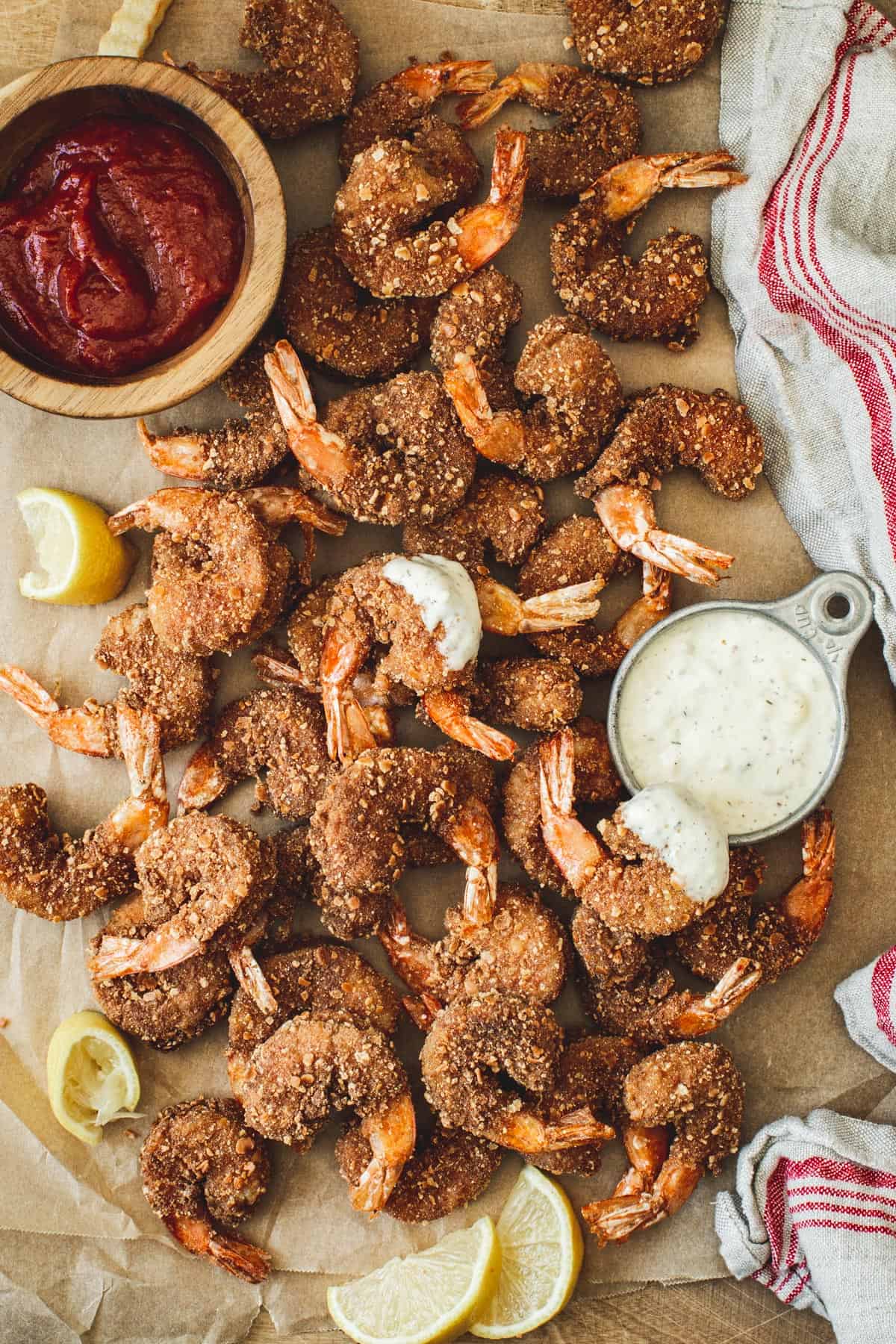 Crispy breaded shrimp piled on parchment with cocktail sauce and tartar sauce.