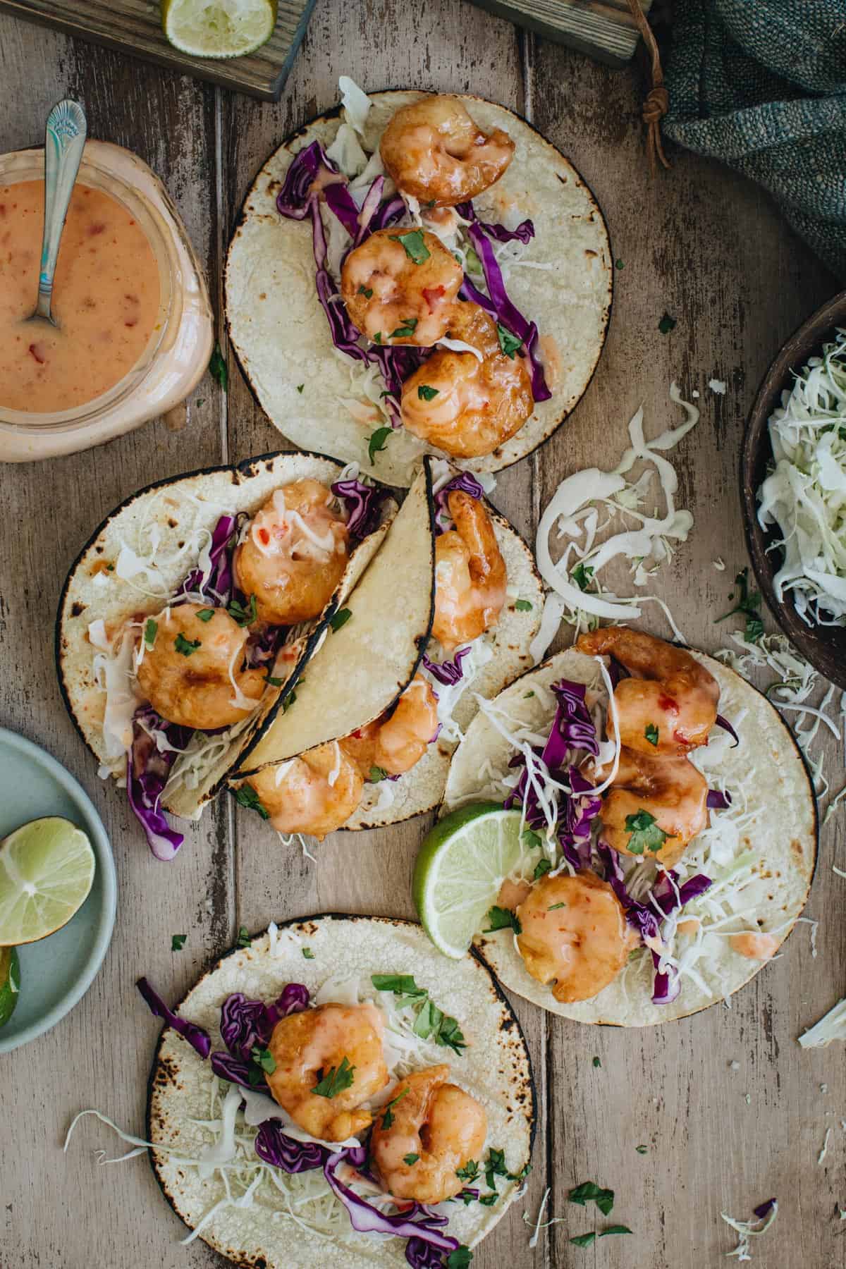 Bang bang shrimp tacos covered in bang bang sauce on a wooden table.